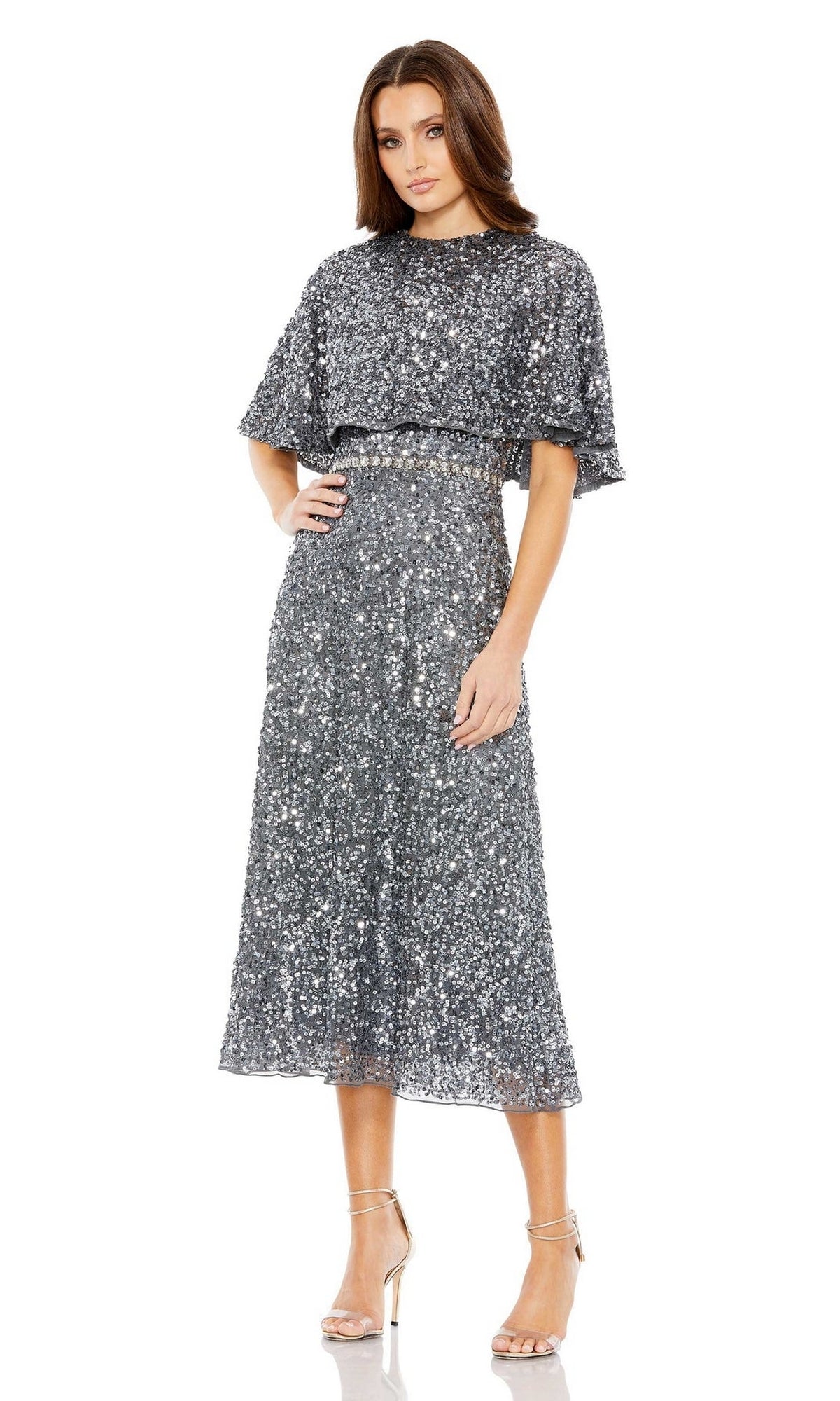 A woman stands wearing the Mac Duggal 5577 Caped Midi Semi-Formal Dress with short sleeves and a belted waist, paired with strappy high-heeled sandals.